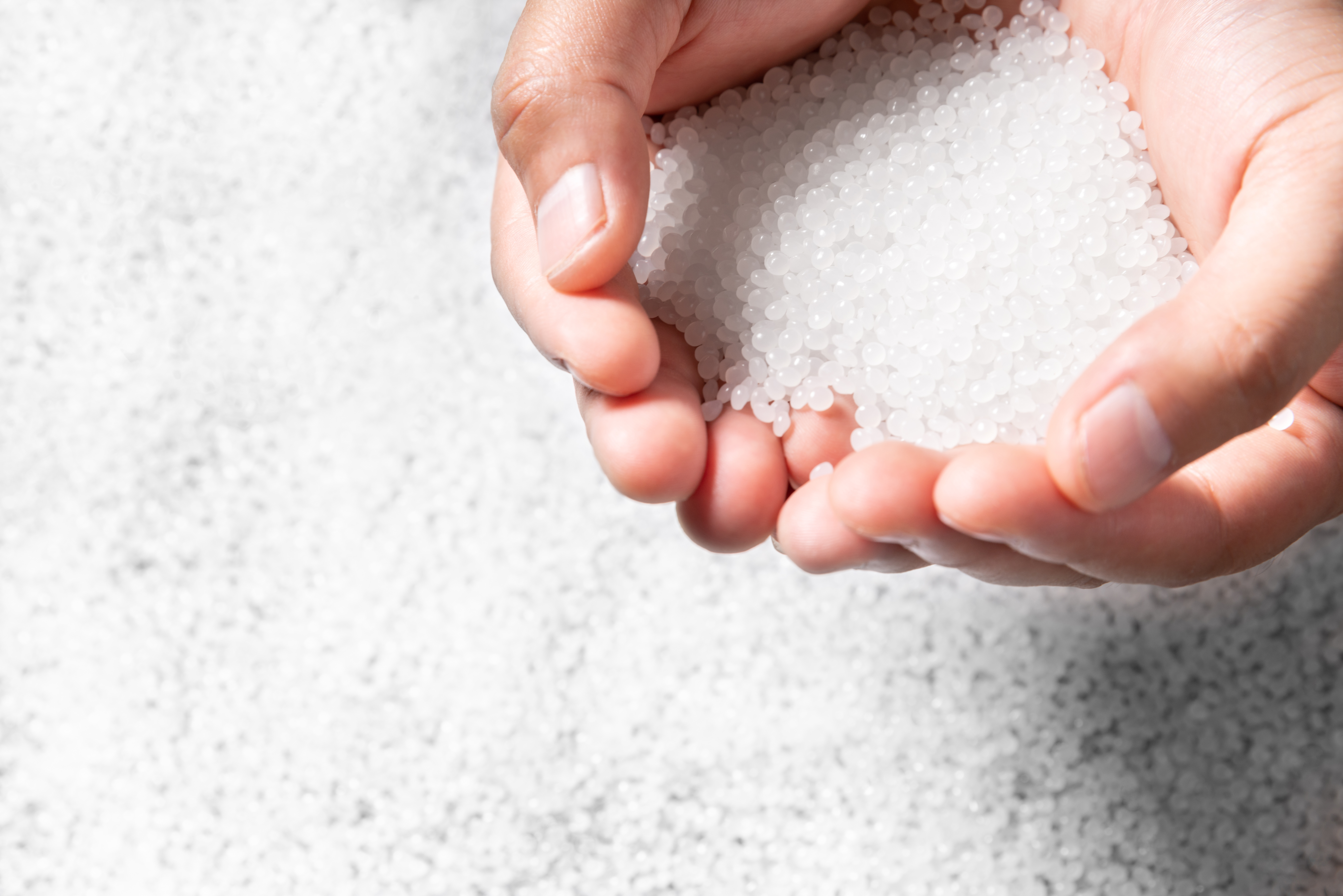 Close-up of cupped hands holding white PVC polymer granules, with more pellets in the background